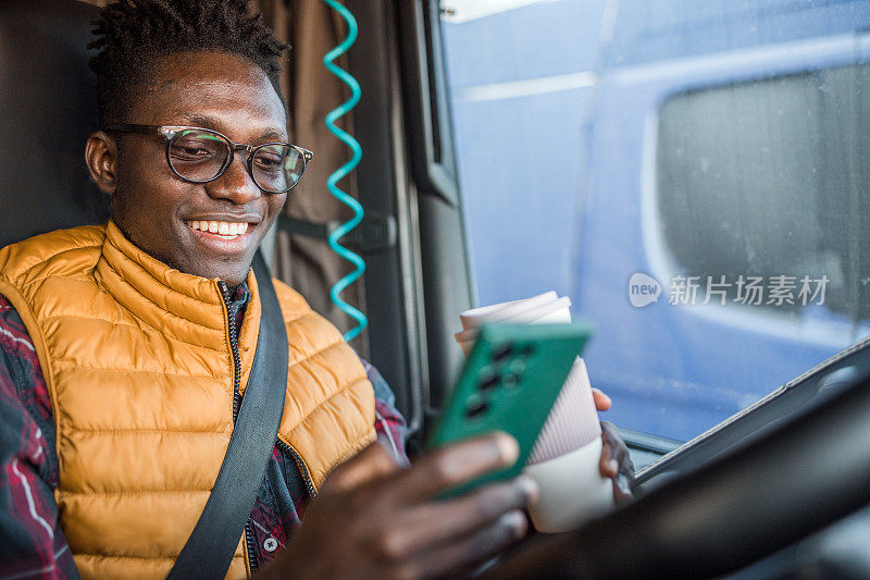 快乐的男卡车司机在开车休息的时候用手机上网，用一次性杯子喝咖啡