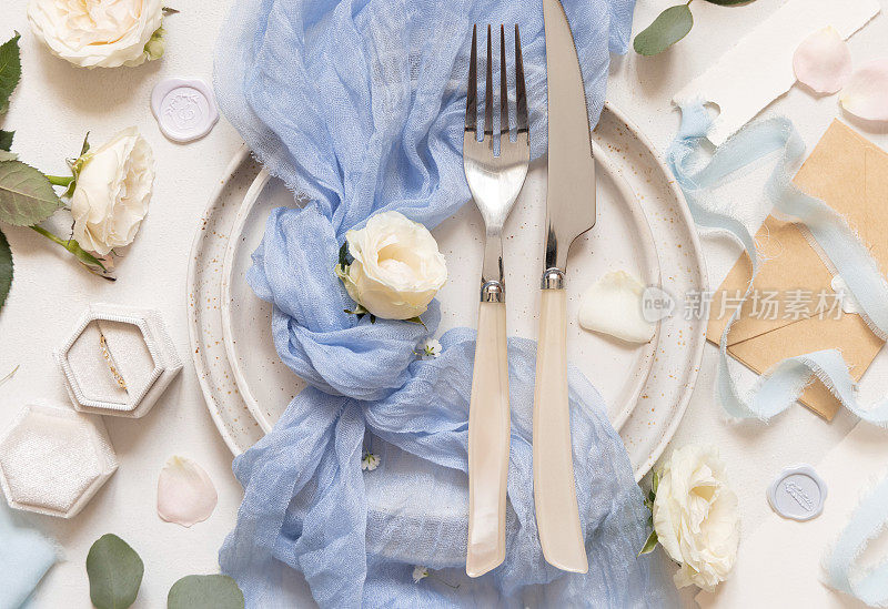 婚礼餐桌上摆放着用刀叉、蓝色薄纱织物和奶油色花朵的顶景