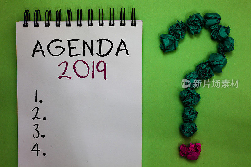 文字标志显示2019年议程。打开笔记本，皱巴巴的纸，形成绿色问号背景。