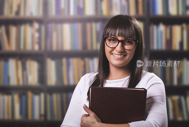 一个漂亮的微笑的女孩在图书馆看书的肖像