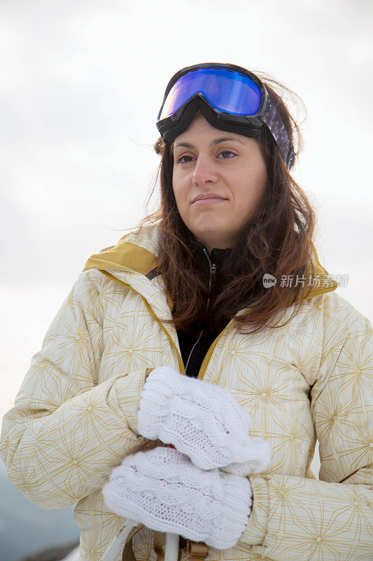 近景美丽的年轻女子在冬天的衣服站在一边，手拿木棍的背景雪山