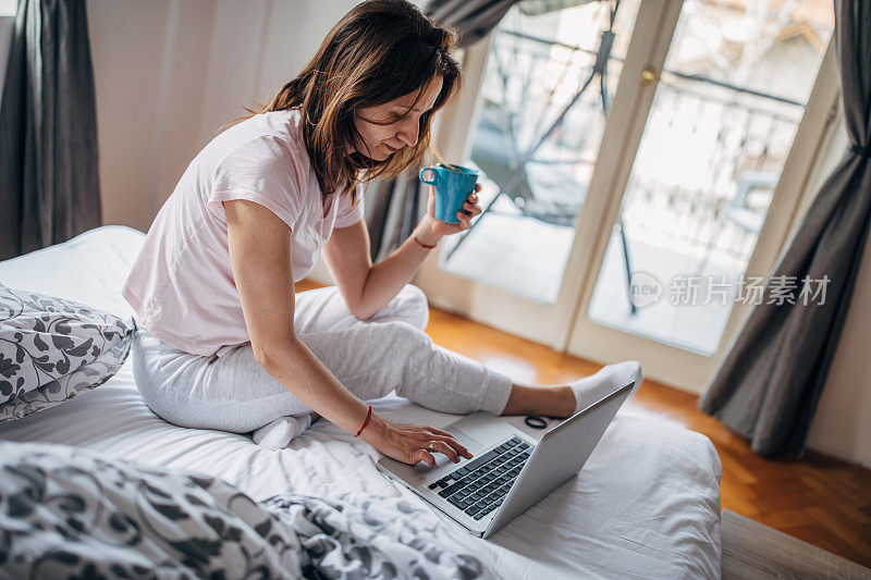 女人在床上用笔记本电脑和喝咖啡