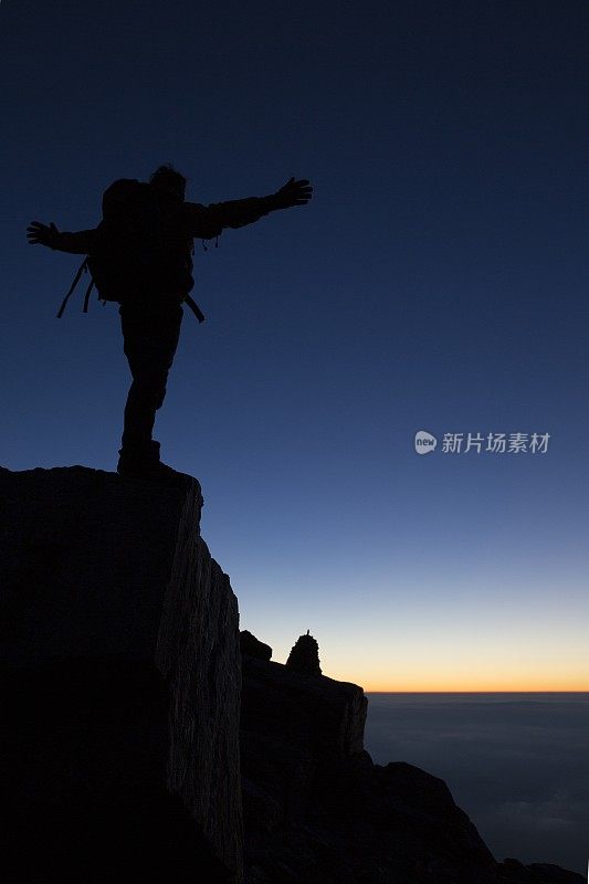 一个徒步旅行者伸出双臂站在岩顶的剪影上