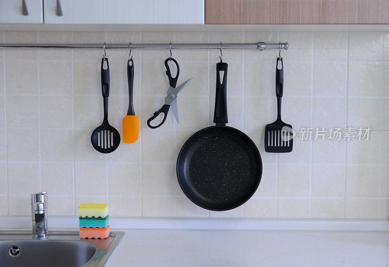 不粘锅，用来装食物的剪刀，用来翻牛排的铲子，以瓷砖为背景的勺子，厨房的内部。