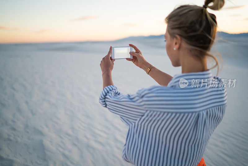 年轻女性游客在智能手机相机上自拍探索白色沙丘，嬉皮女孩旅游拍日落风景享受度假手机相机