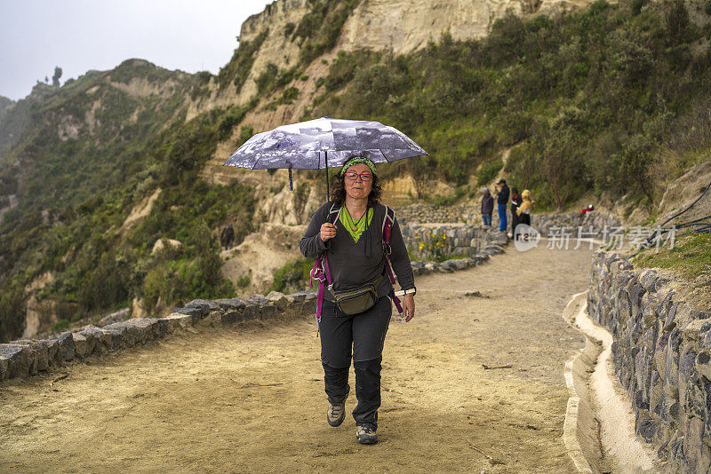 在厄瓜多尔基洛托阿火山火山口徒步旅行的女人，带着伞，在雨中行走