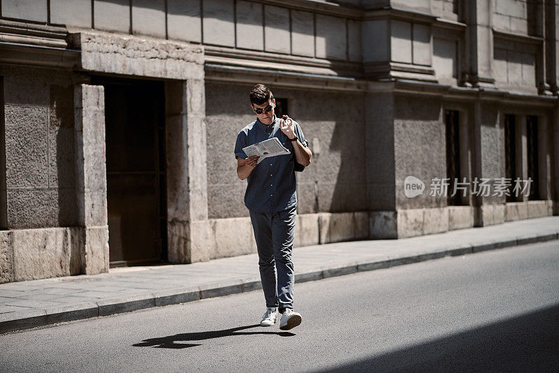 在阳光明媚的日子里，年轻英俊的男子拿着报纸走在街上。年轻的商人在城里忙了一天。
