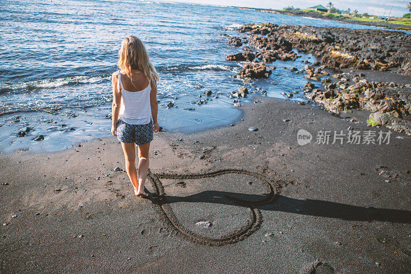 年轻的女人在黑色的沙滩上靠近画心
