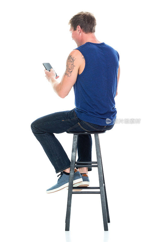 白人男性无袖坐着穿裤子和使用智能手机