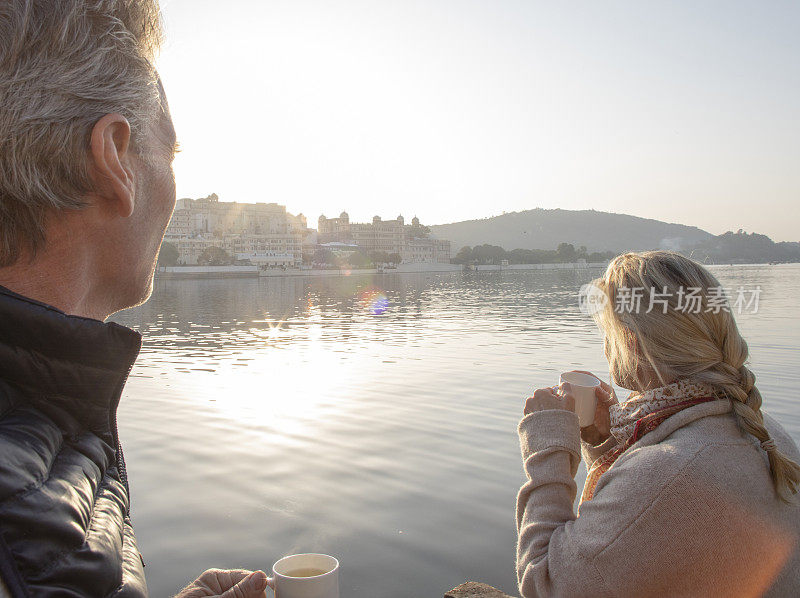 一对成熟的夫妇在日出时带着热饮探索高堤，一边喝着热饮，一边眺望湖面