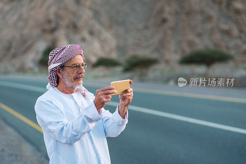 一个阿拉伯人在沙漠的山路上用手机拍照