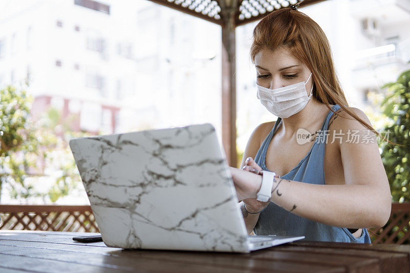 年轻女子戴着面罩，在自家的花园里干活，把自己隔离开来