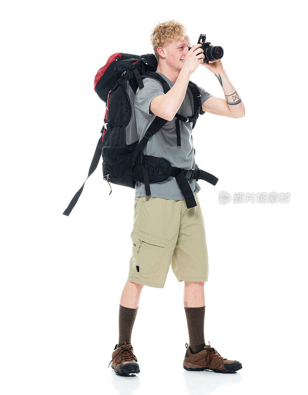 白人年轻男性摄影师徒步旅行在白色背景下，背着背包和拿着相机