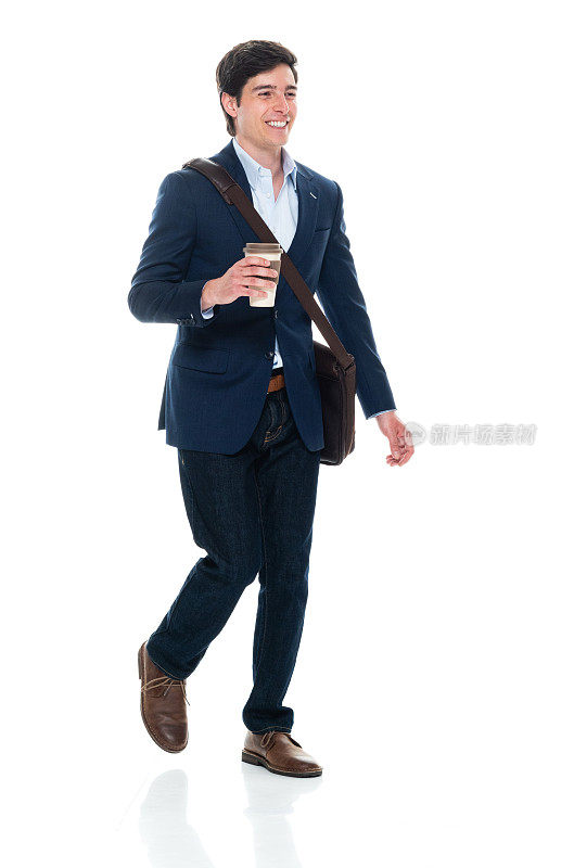 白人年轻男性商务人士走在前面的白色背景，穿着信使包和拿着咖啡杯