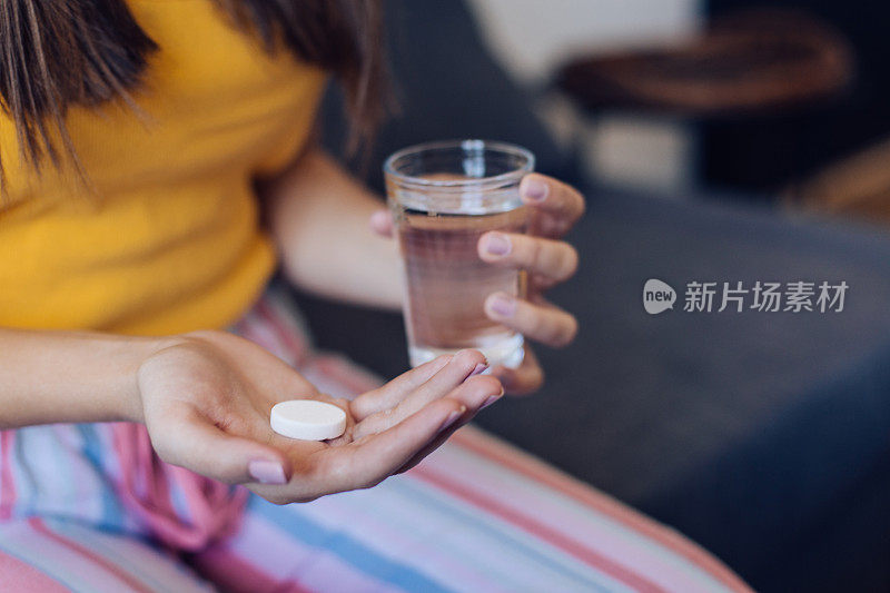 一个不认识的女孩得了流感，拿着冒泡的药片和一杯水;近距离