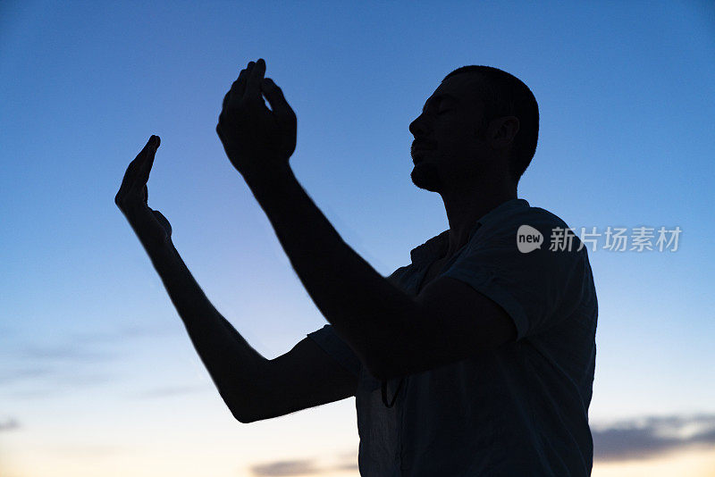 日落时分，穆斯林男子在山顶祈祷的剪影