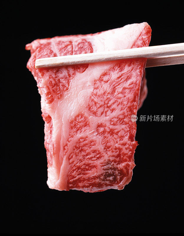 筷子夹着鲜肉片，黑色背景