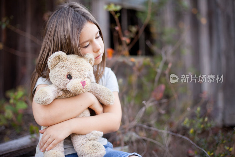 悲伤的年轻女孩拥抱老，破烂的泰迪熊