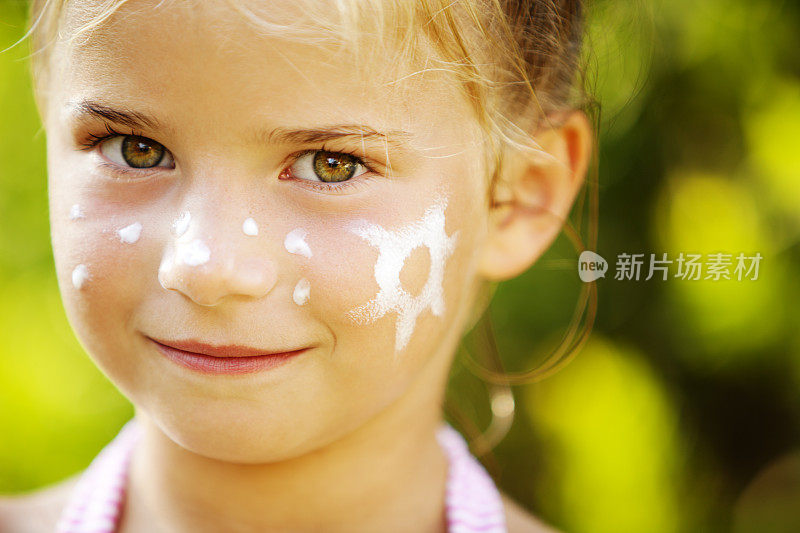 女孩用防晒霜涂抹在她的脸颊上，以太阳的形状