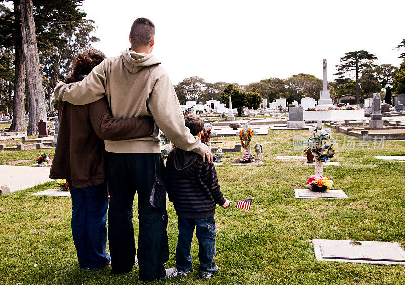 一家三口站在墓地的草地上互相拥抱