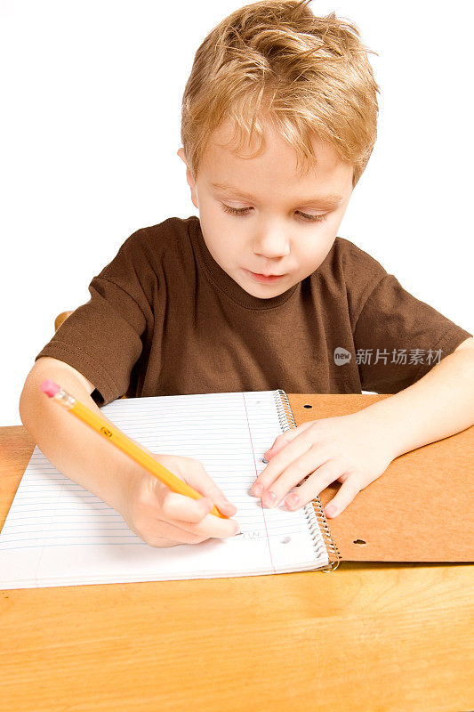 用铅笔在书桌上写笔记本的男孩