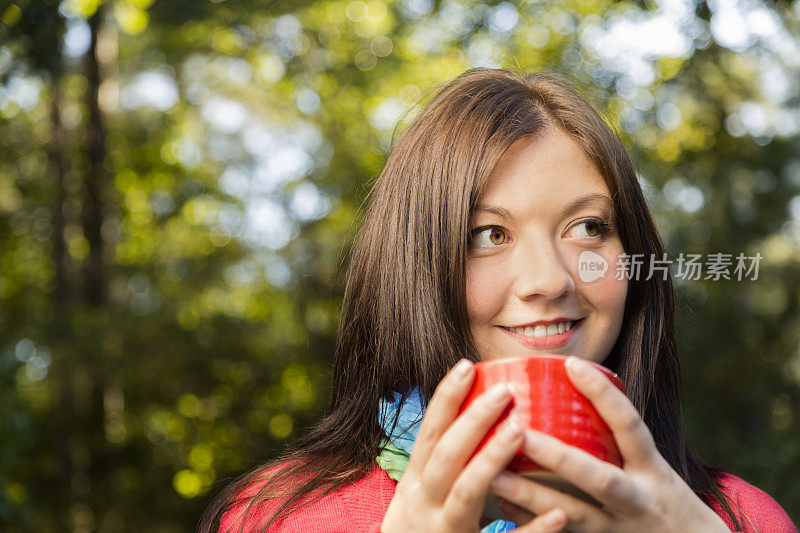 饮品:一名年轻女子在秋天的室外端着热咖啡
