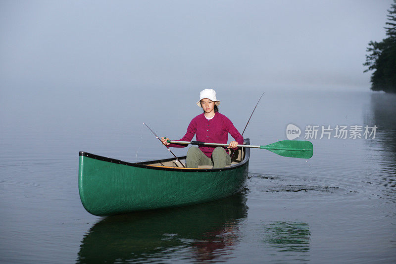 户外女孩划着独木舟在薄雾清晨的湖上钓鱼