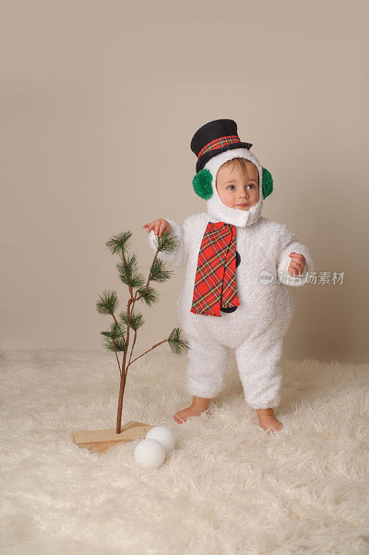 穿着雪人服装的婴儿站在光秃秃的圣诞树旁