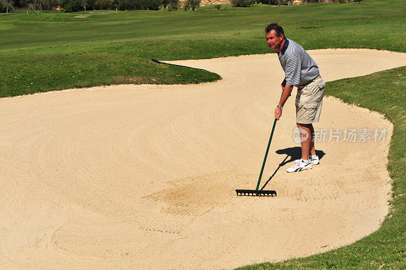 高尔夫球手在沙坑使用后用耙子耙。