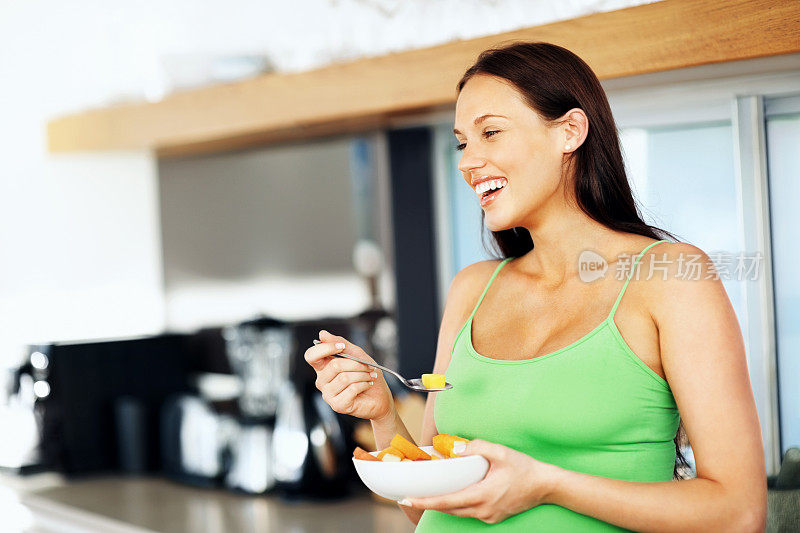 微笑的孕妇拿着一碗水果沙拉