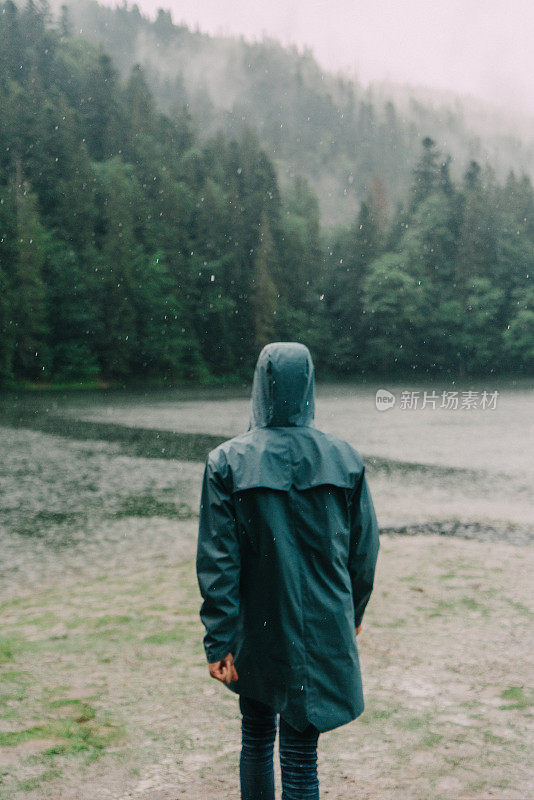 在倾盆大雨中，穿着雨衣的人站在湖边