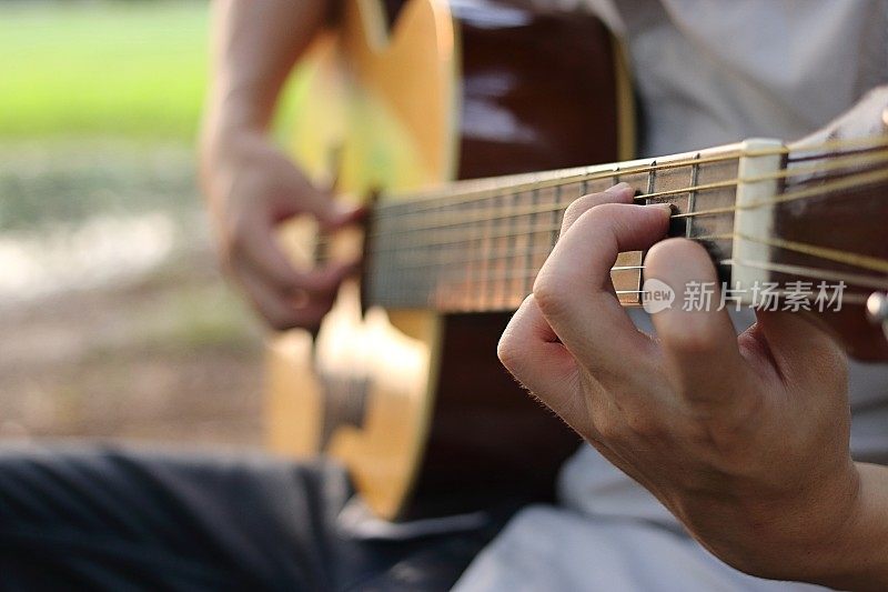 吉他手在模糊的自然背景上选择性的聚焦原声吉他手的手指。