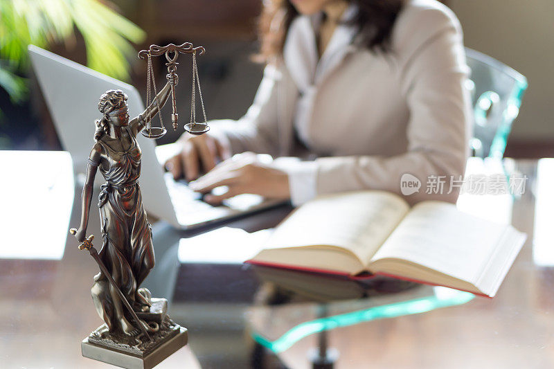 律师的办公室。带天平的正义雕像和在笔记本电脑上工作的律师。法律、法律咨询和司法理念