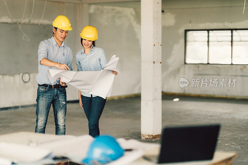 年轻的亚洲工程师夫妇工作在建筑工地的建筑蓝图。土木工程，工业，或家庭装修概念。与复制空间