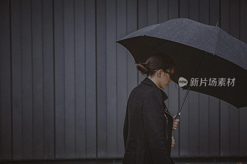 一名年轻女子撑着伞，在寒冷的秋日里在风雨中行走。