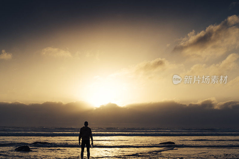 一名男子沿着海滩跑步后，站在日落时分的海滩上。