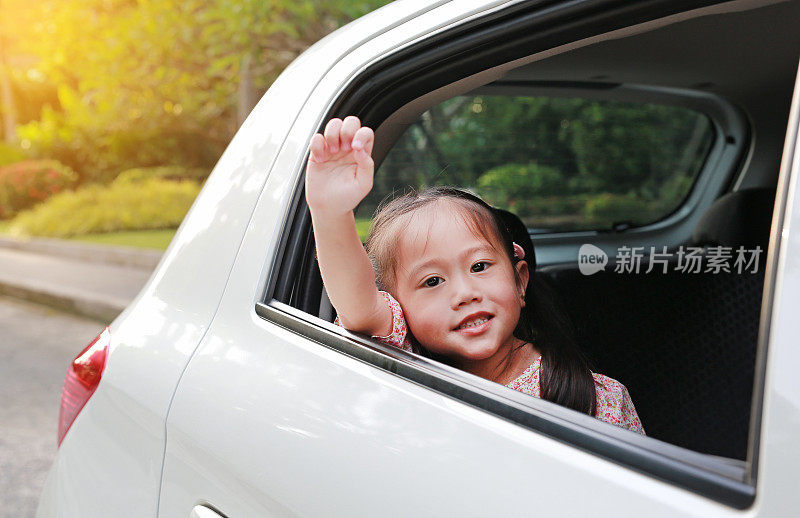 可爱的亚洲小女孩看着镜头从车窗与光线的汽车。