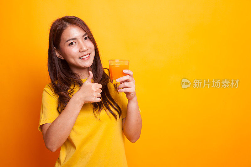 年轻的亚洲女人拇指喝橙汁在黄色的裙子