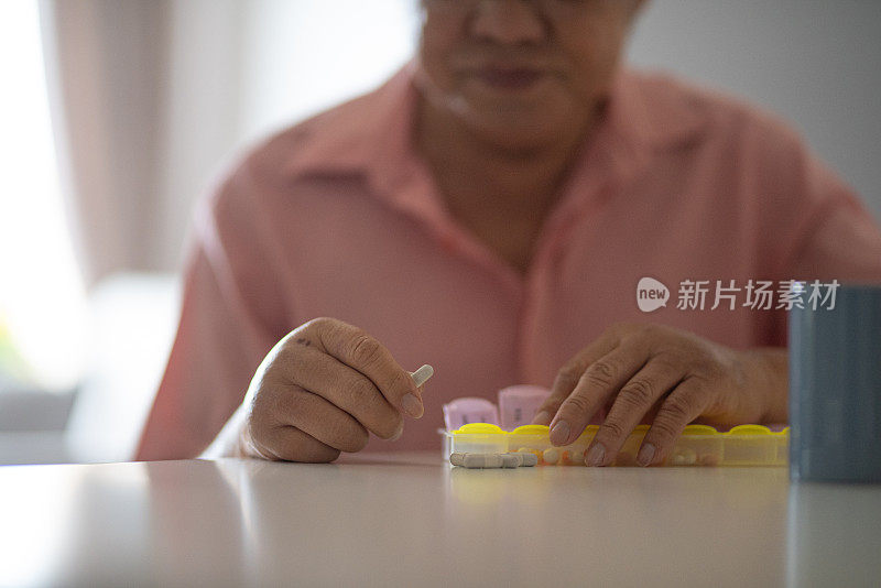 一名亚裔华人老人正在把药品放在药片收纳器里