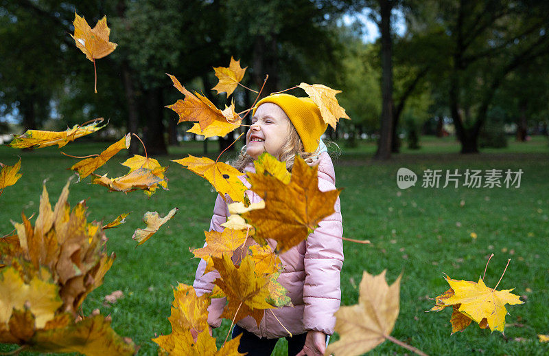 一个孩子在公园里玩黄色的枫叶。