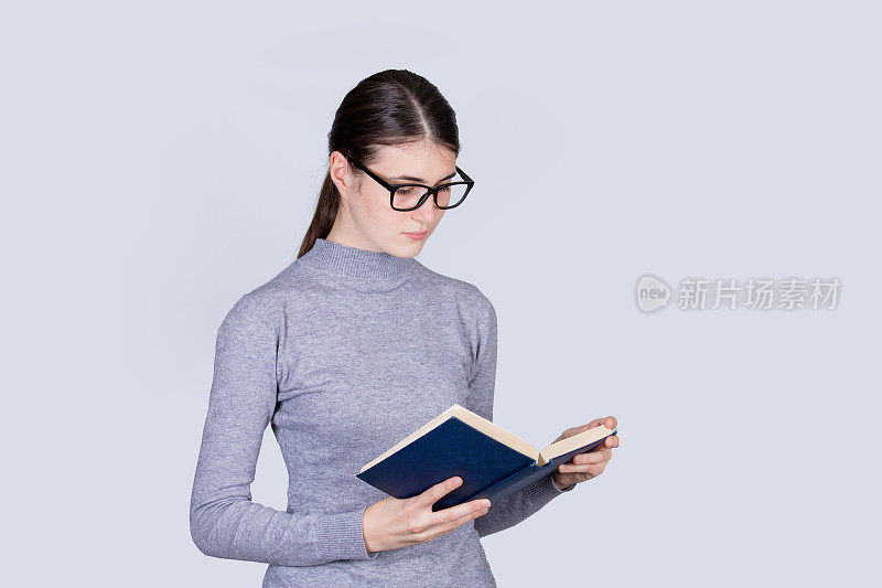 困惑的女学生在书中看着悲伤。困惑的学生女孩读一本教科书孤立在白色的背景。