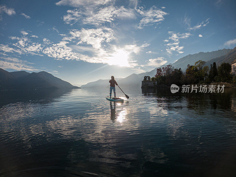 日落时分，女人在湖上站立式划桨板上划水