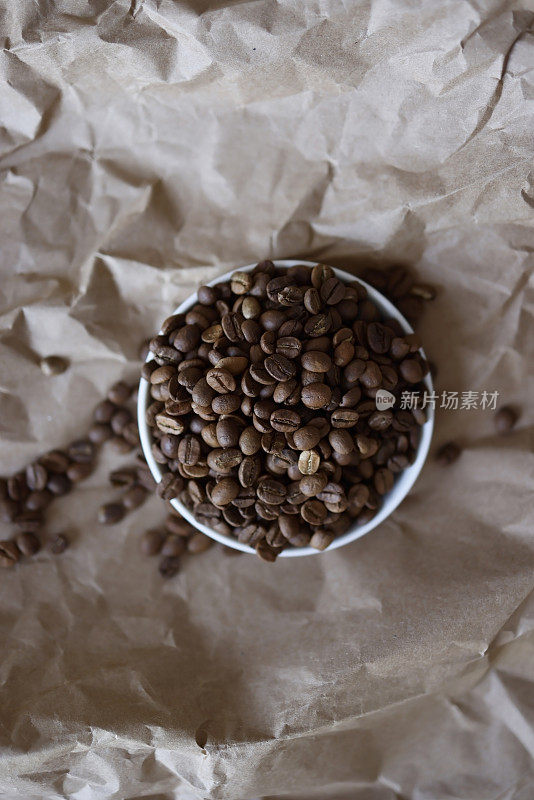 咖啡豆放在白色的圆盘子里，棕色的包装纸上，包装纸被弄皱了，咖啡豆散落在纸上