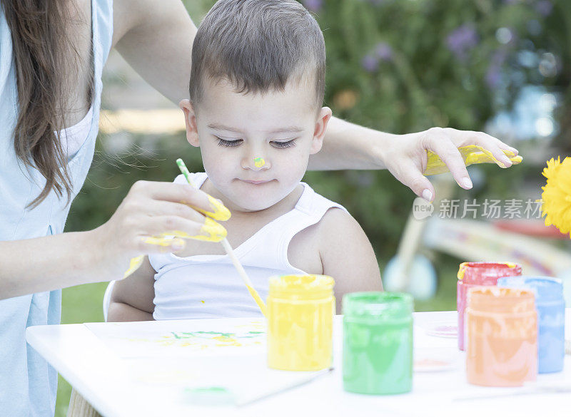 一个可爱的小男孩用画笔画画。绘画的乐趣。一个小男孩在家里的花园里画画。