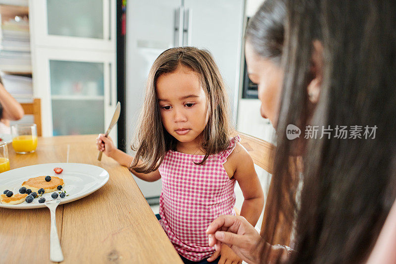 一个可爱的小女孩和她的妈妈在家里吃煎饼当早餐