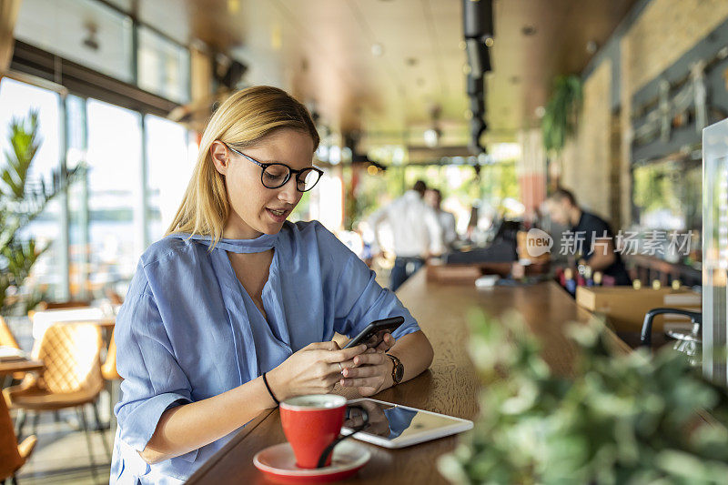 一个非常有吸引力的年轻女商人正在Café享受热饮，并在她的手机上做一些商业计划。