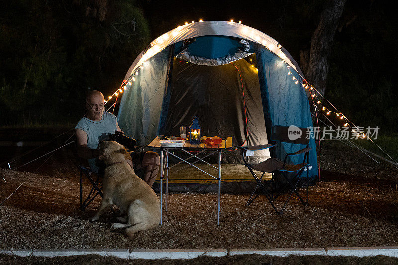 高级摄影师放松与他的狗，而他在露营