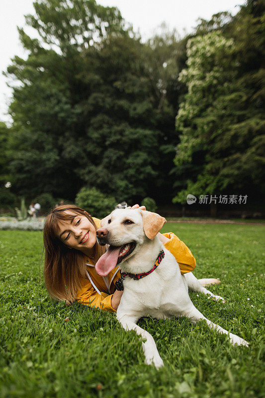 一个年轻漂亮的女人和她的拉布拉多狗躺在草地上