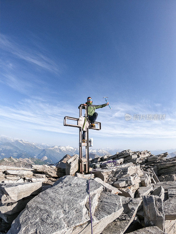 登山者坐在山顶的十字架上凝视着山顶的景色