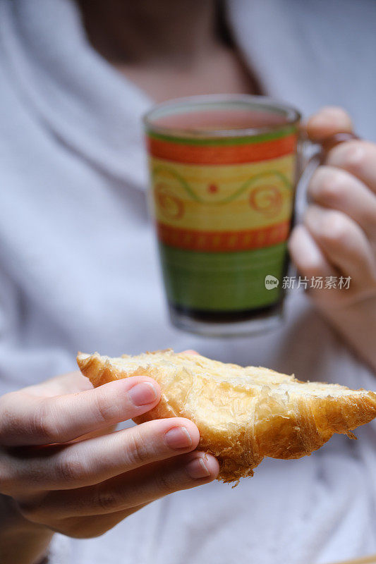 成熟女人手里拿着一杯咖啡和羊角面包